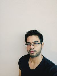 Portrait of young man wearing eyeglasses against wall