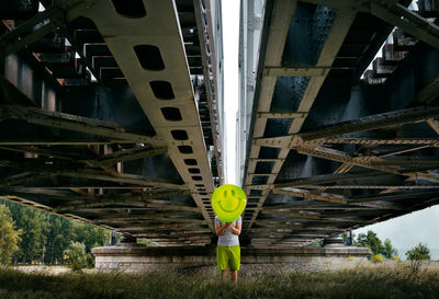 Front view of man with balloon standing under railway bridge