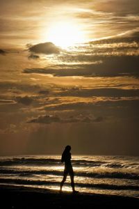 Silhouette people walking on beach against sky during sunset