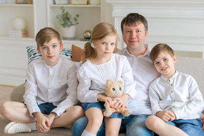 Cheerful father with laughing children looking at camera sitting on couch