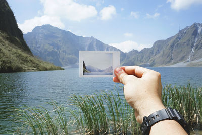 Scenic view of hand holding photograph in front of lake