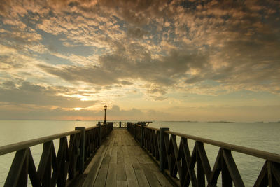 Jetty leading to sea against cloudy sky