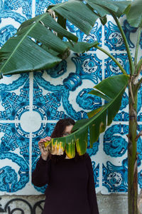 Portrait of woman holding banana leaf by patterned wall