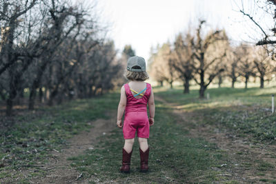 A young girl stands in an orchard wearing a leotard and cowgirl boots.