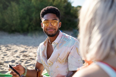 Black man sharing news in social media with anonymous girlfriend while spending time on sandy beach against sea and blue sky together