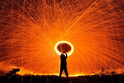 Silhouette man spinning illuminated wire wool at night