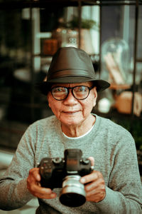 Portrait of senior man holding camera while sitting in cafe