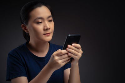 Young woman using mobile phone against black background