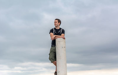 Young man standing by pole against sky