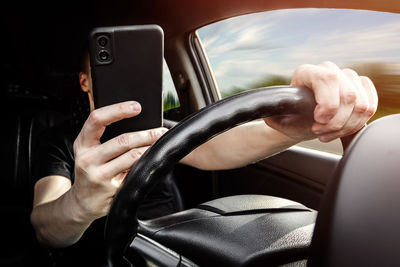 Midsection of man using mobile phone while driving car