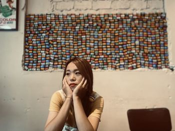 Young woman looking away while sitting against wall