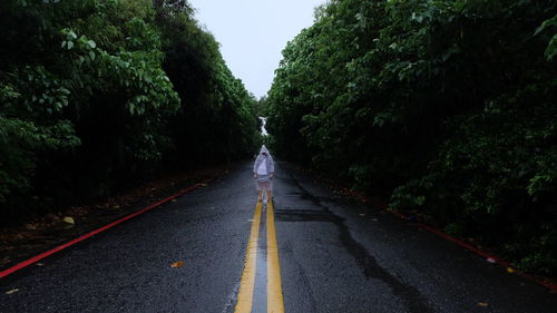 Person with raincoat standing on wet street amidst trees