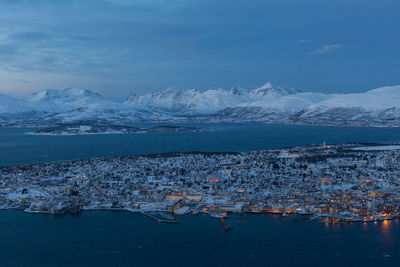 Town by fjord with snowcapped mountains against sky