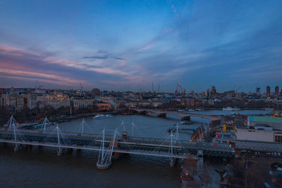 Bridge over river in city against sky during sunset