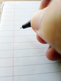 Close-up of hand holding paper with pen on table