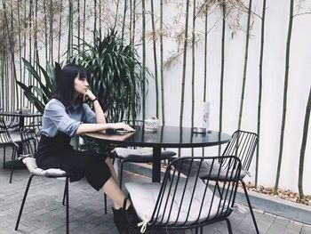 Full length of woman sitting at table against wall at restaurant