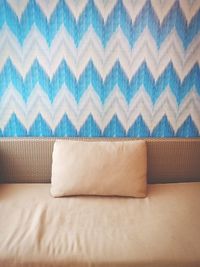 Close-up of cushion on sofa against blue patterned wall at home
