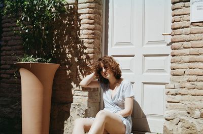 Portrait of smiling young woman sitting against wall