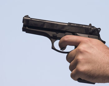 Cropped hand holding gun against sky