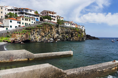 Low angle view of buildings on cliff by sea against sky