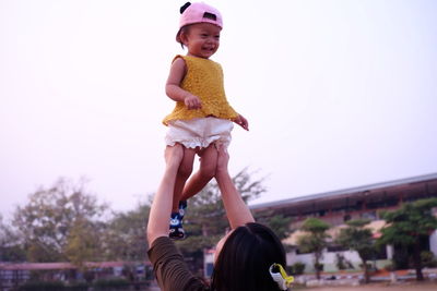Woman lifting girl against clear sky