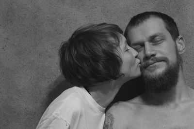 Close-up of girlfriend kissing shirtless boyfriend standing against wall