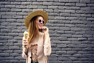 Young woman wearing sunglasses standing against brick wall