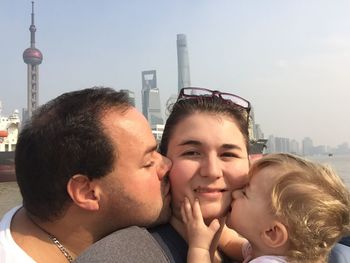 Close-up of father and son kissing woman on cheek against oriental pearl tower