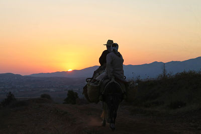 Man riding horse on landscape during sunset