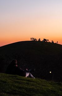 People sitting on field against clear sky during sunset