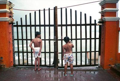 Full length of shirtless kids standing by beach gate