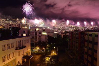 Firework display over illuminated city against sky at night