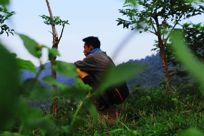 Man crouching on field against sky