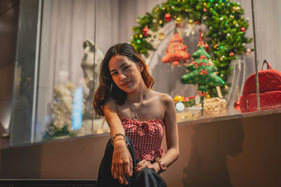 Portrait of young woman standing by christmas tree at home