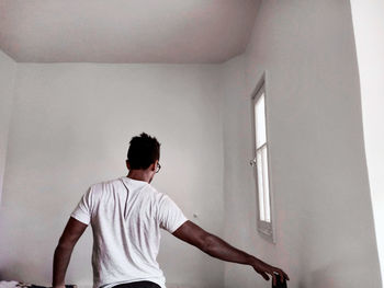 Rear view of man standing against wall at home