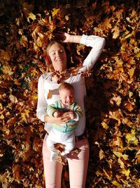 High angle view of baby and mother lying in autumn leaves