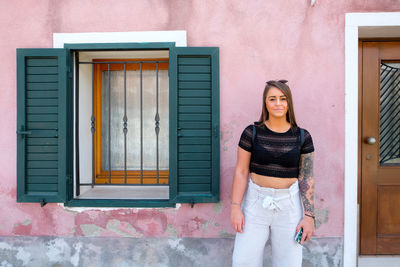 Portrait of young woman standing against building