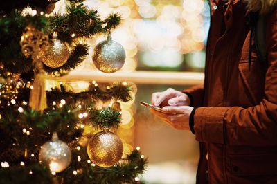 Midsection of man using smart phone against illuminated christmas tree