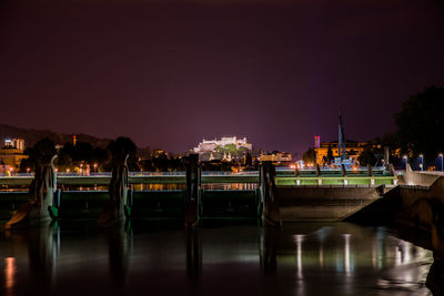 Illuminated bridge over river against sky at night