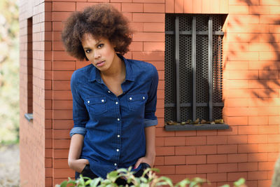 Portrait of young woman leaning against brick wall