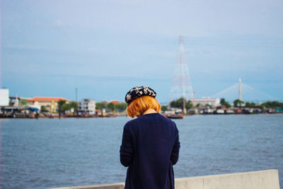 Rear view of woman standing by river against sky