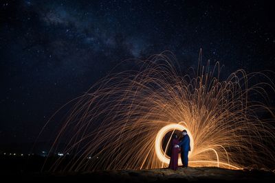 Full length side view of couple standing face to face by spinning wire wool against star field at night