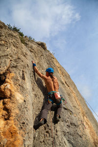 Low angle view of shirtless man rock climbing against sky