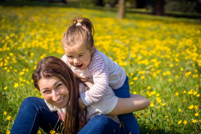 Beautiful woman with daughter sitting and playing on grass at park