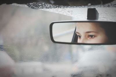 Close-up of woman face reflecting in rear-view mirror