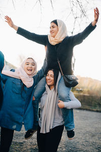 Young woman carrying teenage girl on shoulders by friends against clear sky