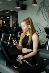 Young woman using mobile phone while exercising at gym