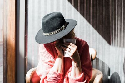 Woman sat hiding under a hat drinking coffee in a cafe in the sunshine