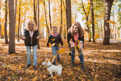 Full length of smiling girl standing by trees during autumn