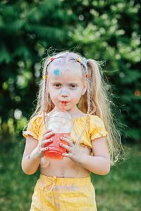 Outdoor portrait of funny grimy little girl with two ponytails drinks lemonade sweet sweetened